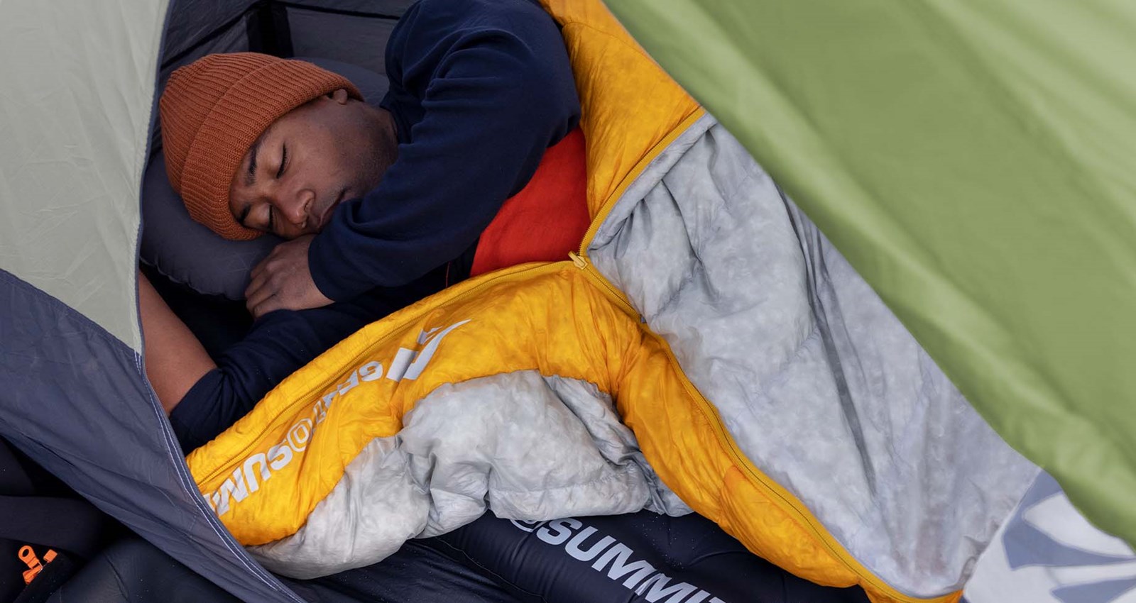PErson der sover i en sovepose inde i et telt.