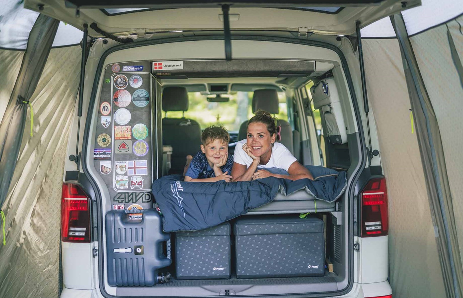 En mor og søn i en camper med biltelt på.