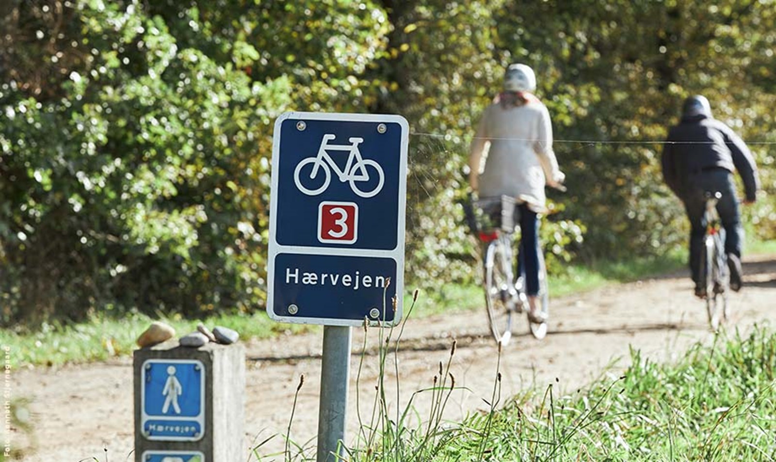 Hærvejen skilt med cyklister i baggrunden.